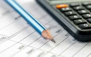 Lápiz azul y calculadora sobre una hoja de cálculo financiera, representando contabilidad y gestión de finanzas